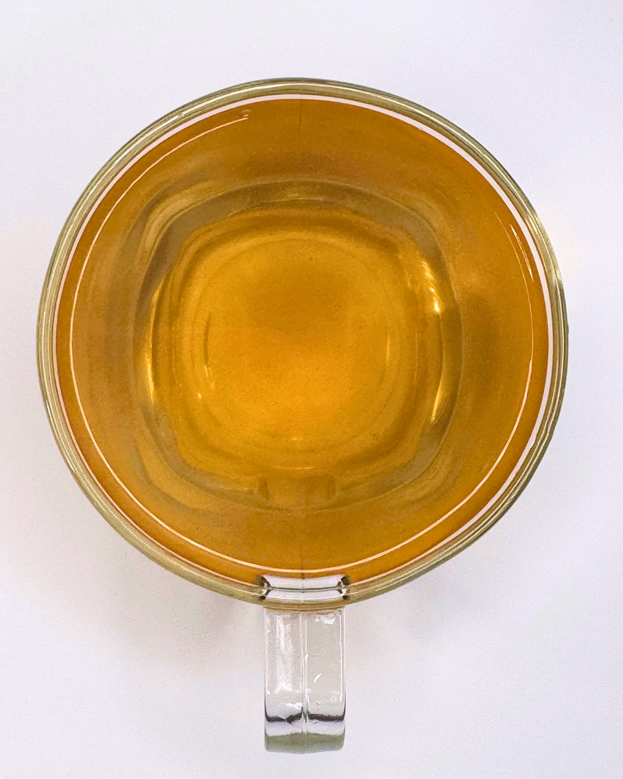 Clear glass mug with a handle filled with a yellowish liquid on a white background